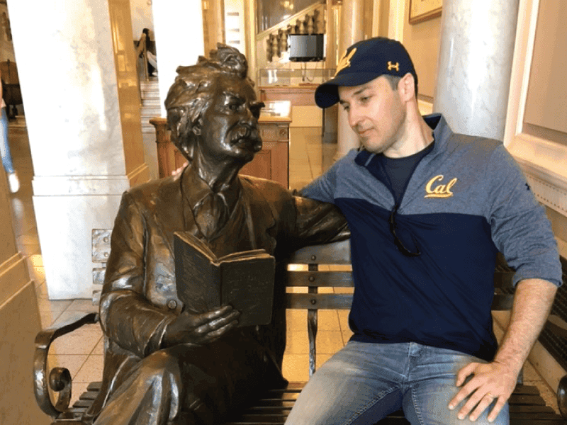 Nick Ostroff at UC Berkeley, in a Cal hat beside the campus statue