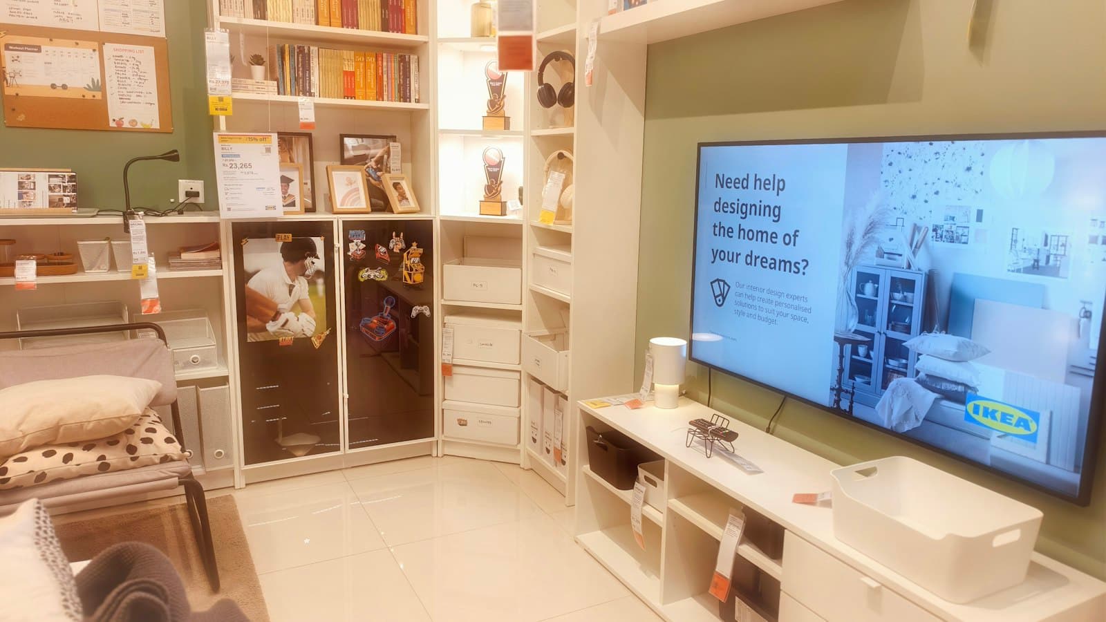 A living room display with white shelving, a television, and storage bins