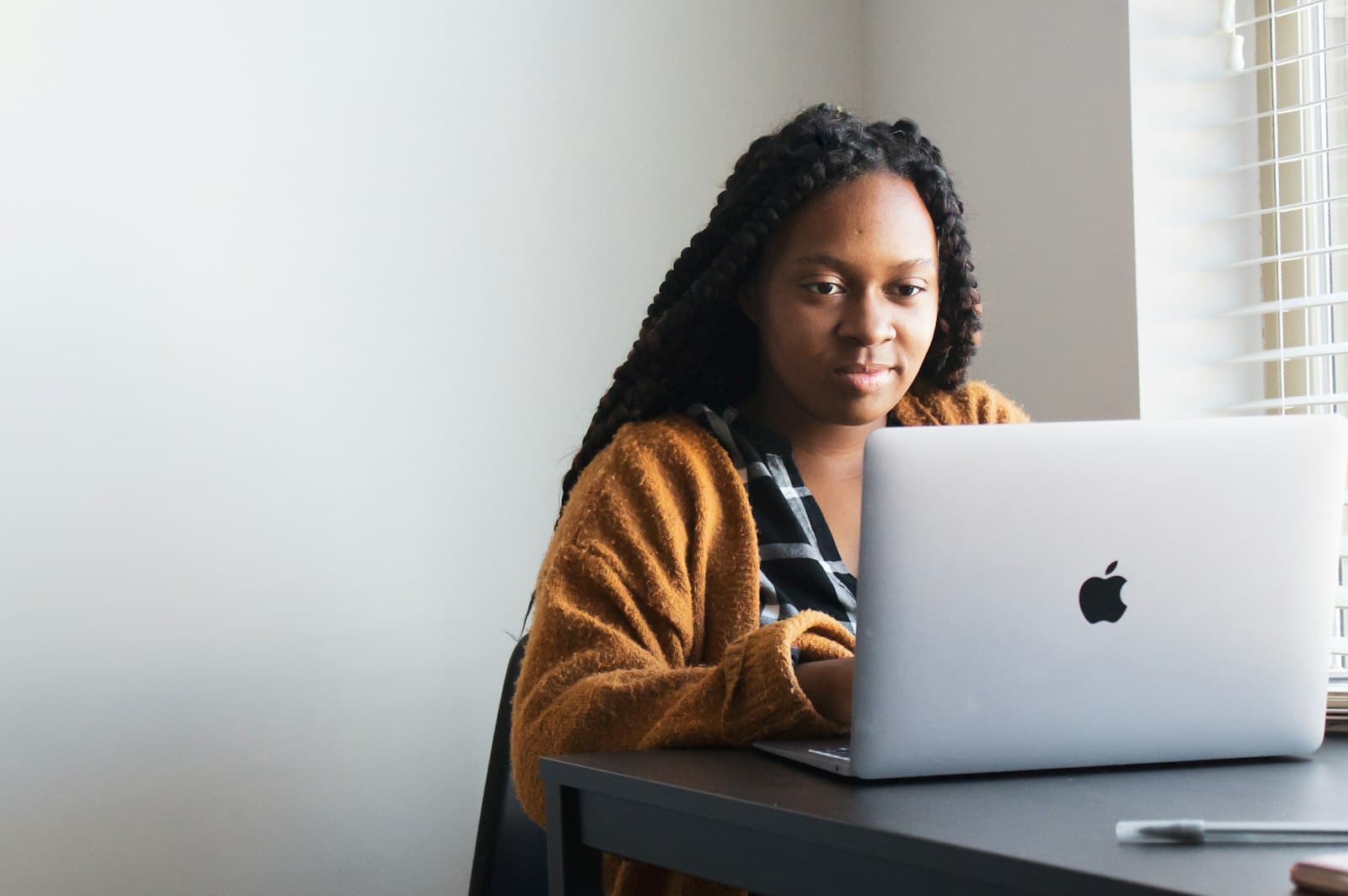 A woman with long braids using a laptop at a desk in a workspace